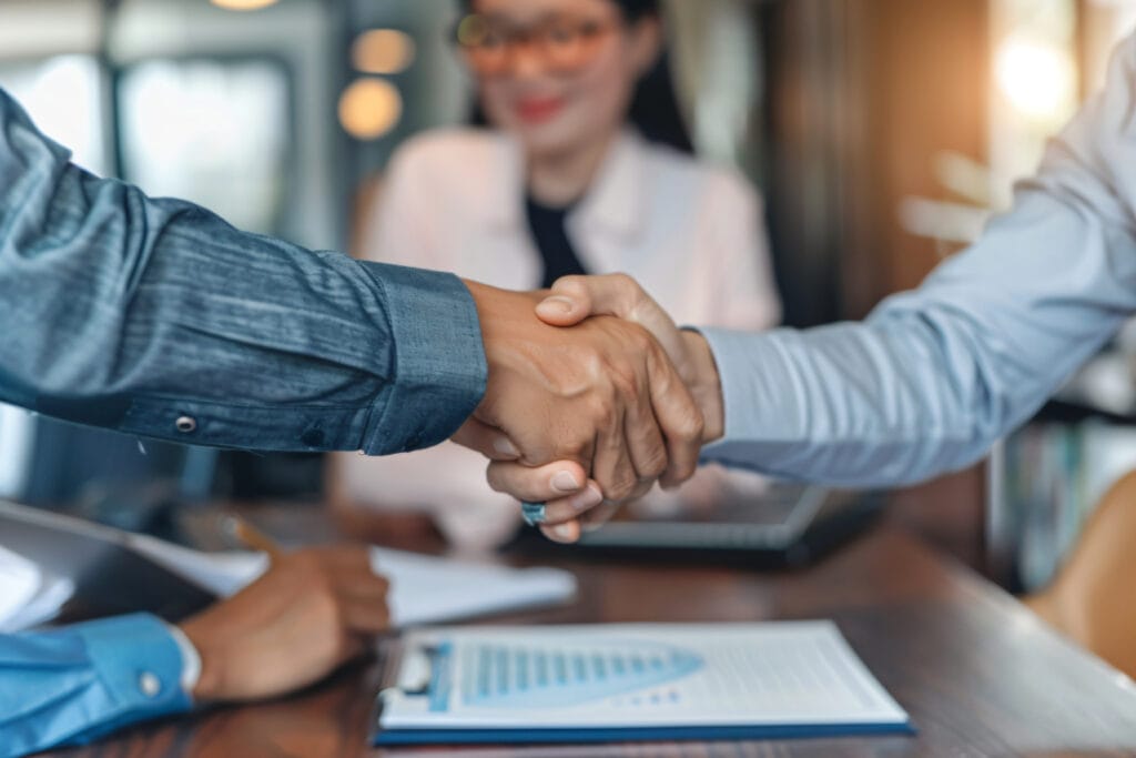 Beneficjenta i przedstawiciel Instytucji wymieniają uścisk ręki po podpisaniu umowy o dofinansowanie projektu